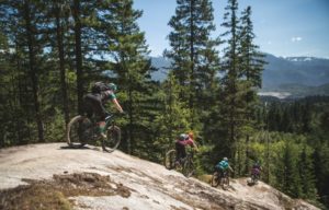 Four female mountain bikers ride a rock slab feature on Bony Elbows mountain biking trail in Squamish, British Columbia.